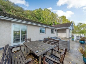 Een huis met een terras, buitenmeubilair en uitzicht op het omliggende groen.
