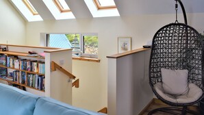 A loft-style room with skylights, a hanging chair, a bookshelf, and a window with a view of greenery. - 4 bedroom accommodation in Portnalong, Isle of Skye (Portnalong, Isle of Skye)