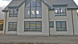 A two-story house with a gabled roof, large windows, and a gravel driveway. - 4 bedroom accommodation in Portnalong, Isle of Skye (Portnalong, Isle of Skye)