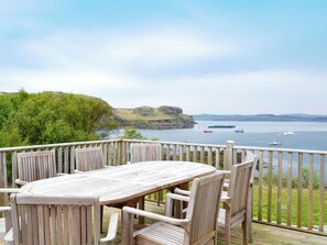 A wooden deck with a table and chairs overlooking a body of water with boats and a distant hill. - 4 bedroom accommodation in Portnalong, Isle of Skye (Portnalong, Isle of Skye)
