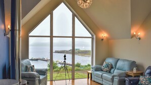A spacious living room with a large bay window overlooking a body of water, a fireplace, and a tripod with a camera. - 4 bedroom accommodation in Portnalong, Isle of Skye (Portnalong, Isle of Skye)