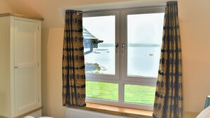 A hotel room with a bed, a window with curtains, a view of the sea, and a white wardrobe. - 4 bedroom accommodation in Portnalong, Isle of Skye (Portnalong, Isle of Skye)