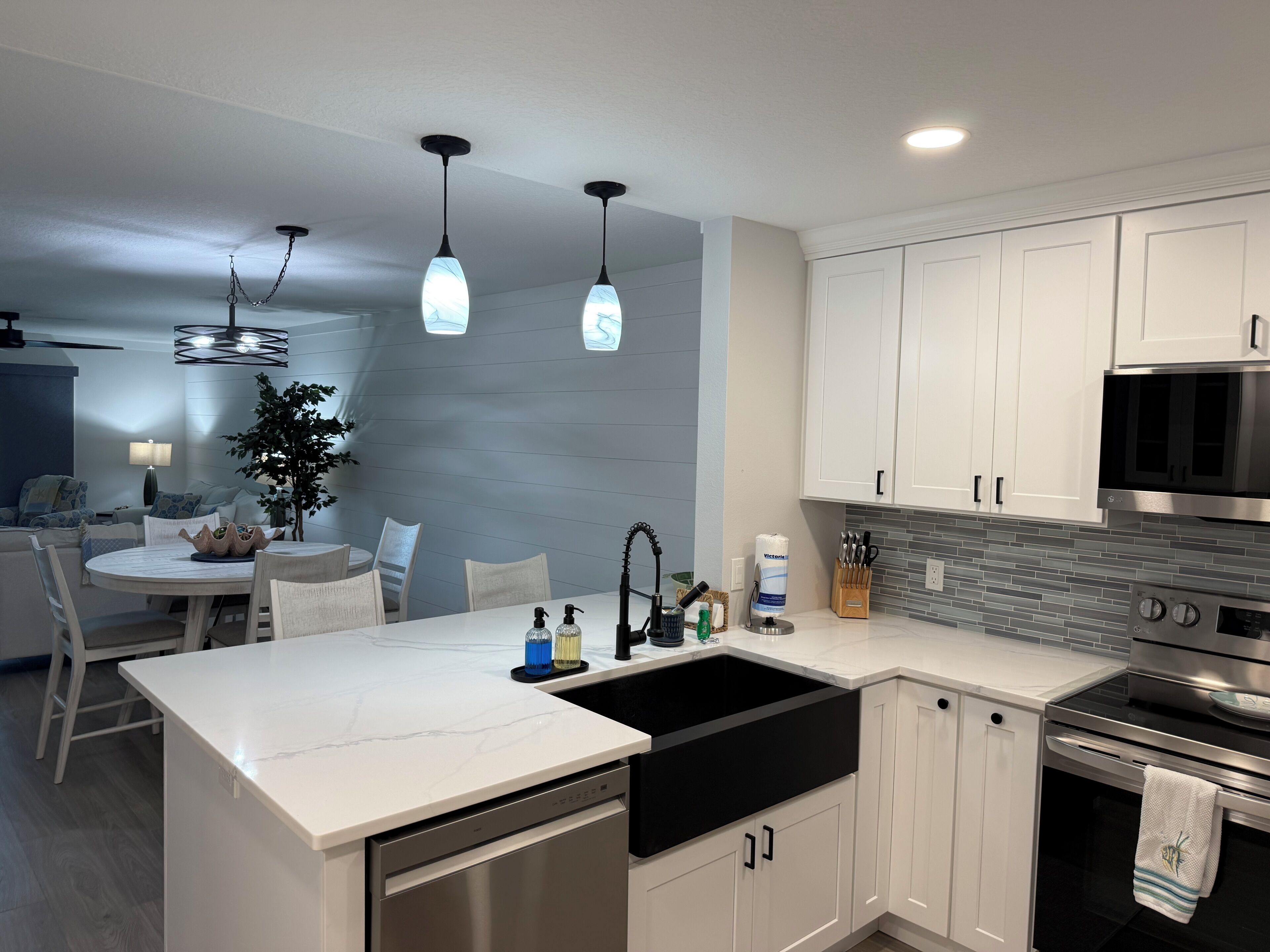 Une cuisine moderne avec des meubles blancs, un évier noir, des appareils en acier inoxydable et des luminaires suspendus.