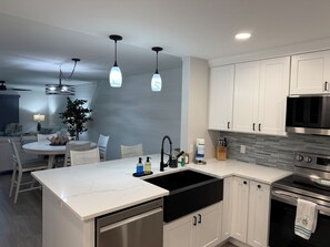 A modern kitchen with white cabinetry, a black sink, stainless steel appliances, and pendant lighting.