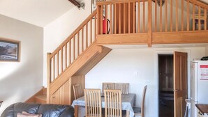 Un comedor con sillas de madera y una mesa, un sofá de cuero negro y una escalera de madera.