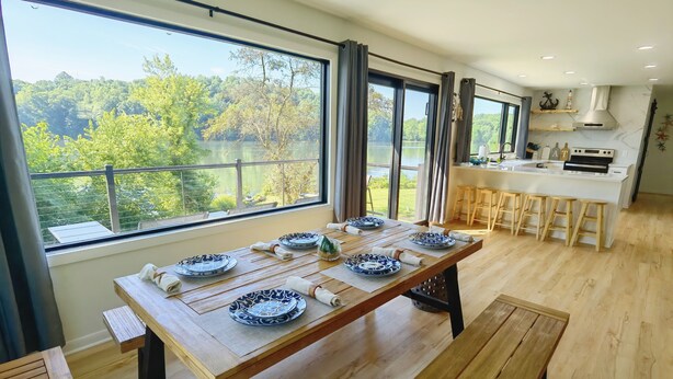 A modern kitchen with a large island, wooden flooring, and a view of a lake.