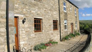 A stone building with multiple windows, a door, and a small garden area with flowers. - 6 bedroom accommodation in Muker (Muker)