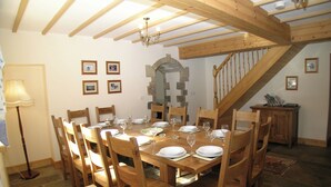A dining room with a wooden table set for six, surrounded by wooden chairs. A staircase with wooden railings is visible in the background. - 6 bedroom accommodation in Muker (Muker)
