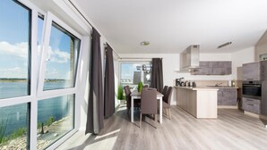 Cozinha moderna com vista para a água, área de jantar com mesa e cadeiras, e uma janela grande com cortinas.