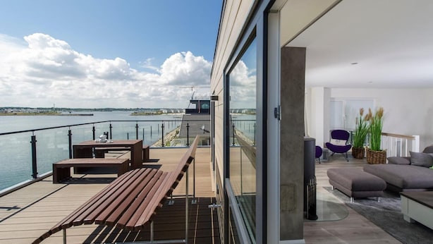 Uma sala de estar moderna com uma grande porta de vidro que dá para uma varanda com vista para um corpo de água.