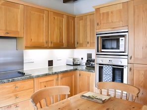 A kitchen with wooden cabinets, a microwave, a toaster, and a table with a book. - Gran's Cottage Askrigg (Askrigg)