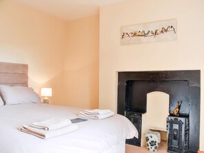 A hotel room with a bed, a nightstand, a lamp, a painting of birds, and a fireplace. - Gran's Cottage Askrigg (Askrigg)
