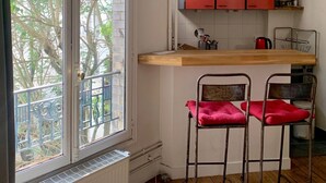 A kitchen with a window, a wooden countertop, two metal chairs with red cushions, and a red cabinet above the counter.