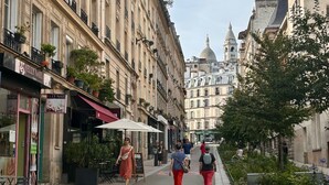 A street with buildings, a woman walking, and a man with a backpack.