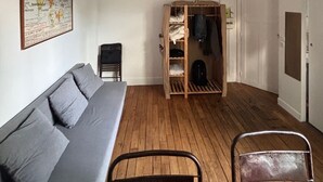 A room with a grey sofa, a wooden coat rack with clothes, a metal chair, and a map on the wall.