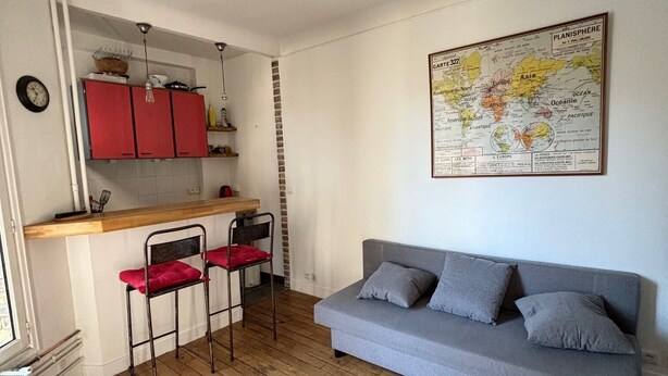 A compact living space with a kitchenette, a grey sofa, and a map on the wall.