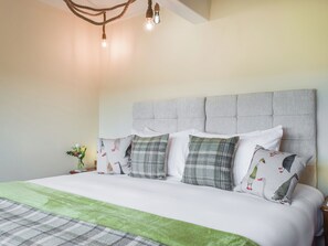 A bedroom with a tufted headboard, a bed with white bedding and green accents, and a bedside table with a vase of flowers.