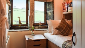 Una habitación con una cama, una mesita de noche, un ventanal con vistas a un campo verde y un estante con cajas.