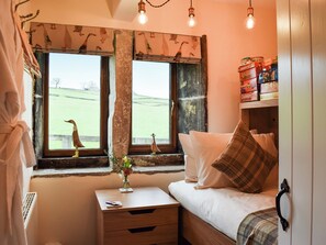 Ein Zimmer mit einem Bett, einem Nachttisch, einem Fenster mit Blick auf ein grünes Feld und einem Regal mit Kisten.