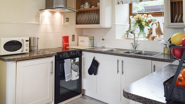 A modern kitchen with a microwave, oven, and sink. There is a window with a view of greenery outside. - 4 bedroom accommodation in Holmfirth (Holmfirth)
