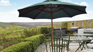 Un patio con un paraguas verde, sillas de metal, una parrilla y una vista panorámica de colinas onduladas.