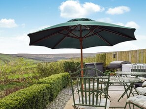 Eine Terrasse mit einem grünen Sonnenschirm, Metallstühlen, einem Grill und einem schönen Blick auf sanfte Hügel.