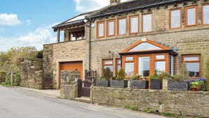 A two-story stone house with a garage, a wooden front door, and a conservatory. - 4 bedroom accommodation in Holmfirth (Holmfirth)