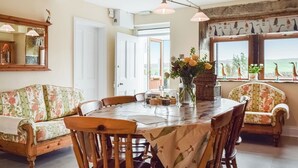 A dining area with a table, chairs, a vase with flowers, and a view through the window. - 4 bedroom accommodation in Holmfirth (Holmfirth)