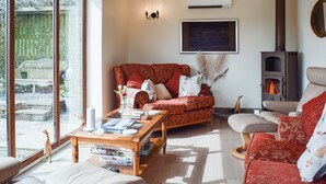 Una sala de estar acogedora con chimenea, un sofá, una mesa de centro con libros y un ventanal grande.