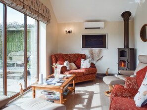 A cozy living room with a fireplace, a sofa, a coffee table with books, and a large window.