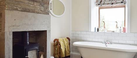 Ein Badezimmer mit einer freistehenden Badewanne, einem Spiegel, einem Kamin und einem Fenster mit gemusterten Vorhängen.