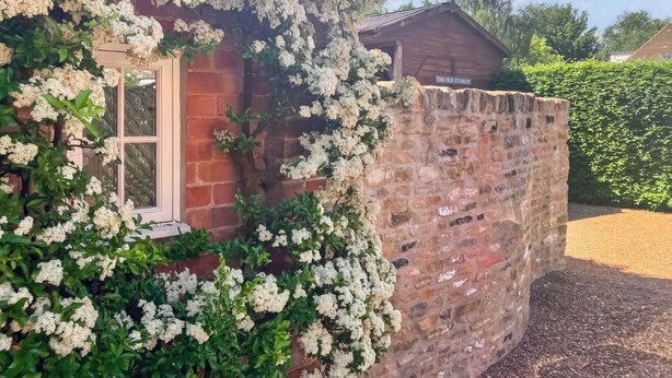 A brick house with a stone wall, a wooden door, and a sign reading 'The Old Stables'.