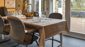 A dining area with a table set for four, chairs, a fruit basket, and a view of a building through a glass door.
