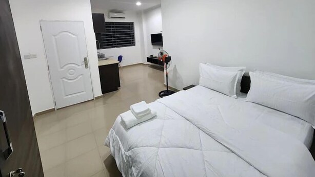 A hotel room with a bed, a desk, a chair, and a TV. - SHEPHERD LINKS APARTMENTS  (Accra)