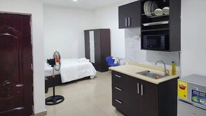 A compact hotel room with a bed, a wardrobe, a small kitchenette with a microwave, and a fan. - SHEPHERD LINKS APARTMENTS  (Accra)