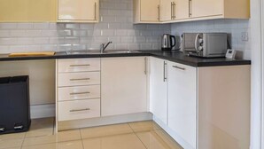 A kitchen with white cabinets, a black countertop, a kettle, a microwave, and a trash bin. - Picked for its character and charm with lots of walks close by. (Llanfynydd)