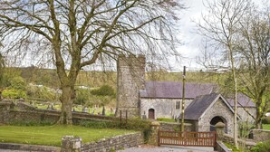A stone building with a sloped roof, a small arched entrance, and a wooden gate. - Picked for its character and charm with lots of walks close by. (Llanfynydd)