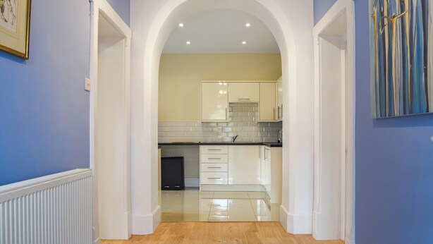 A hallway leading to a kitchen with white cabinets, a tiled backsplash, and a black countertop. - Picked for its character and charm with lots of walks close by. (Llanfynydd)