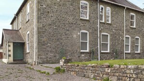 A stone building with a green door, multiple windows with shutters, and a gravel driveway. - Picked for its character and charm with lots of walks close by. (Llanfynydd)