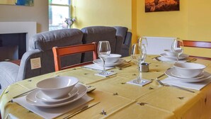 A dining area with a table set for four, including plates, glasses, and cutlery. There are two chairs with cushions, a window with a view, and a painting on the wall. - Picked for its character and charm with lots of walks close by. (Llanfynydd)