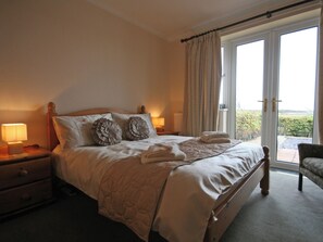 A bedroom with a bed, two bedside lamps, a nightstand, a chair, and a view through a glass door. - An excellent base to explore the North Yorkshire Coast. (Flamborough near Bridlington)