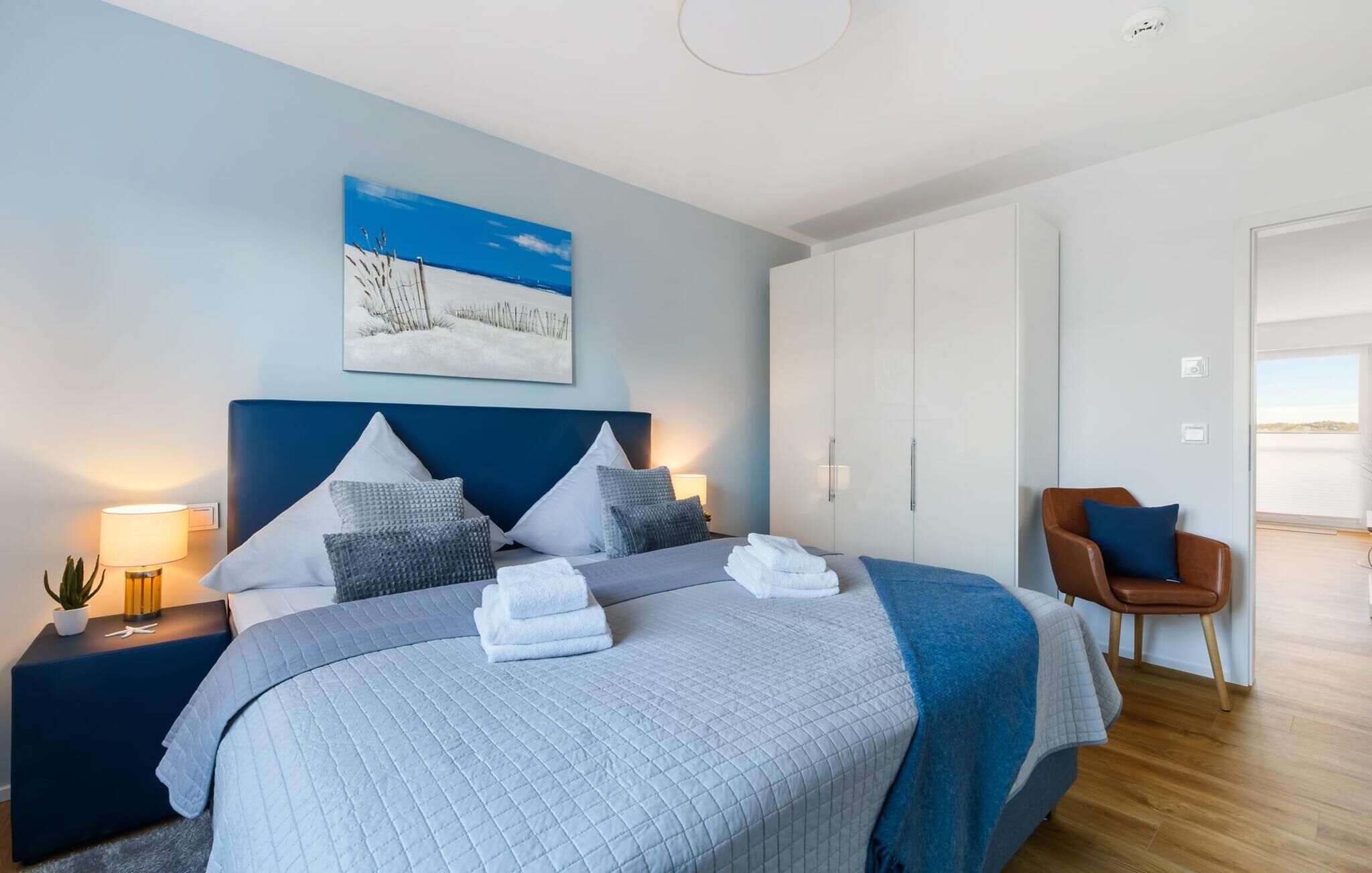 Une chambre à coucher moderne avec un grand lit, une table de chevet avec une lampe, une chaise et un tableau au mur.