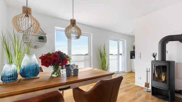 A modern kitchen with a wooden countertop, two hanging pendant lights, a built-in stove, and large windows.