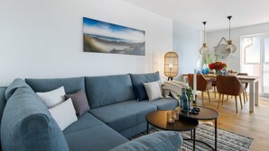 A modern living room with a grey sectional sofa, a round coffee table, and a dining area with a wooden table and chairs.