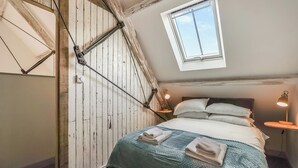 Ein Schlafzimmer mit schrägem Dach, einem Oberlicht, einem Bett mit Kissen und Nachttischlampen.