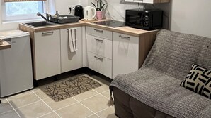 A compact kitchen with a microwave, kettle, and sink. There's a small refrigerator, a sofa, and a patterned rug. - Appartement les Clés de Juliette (Gruissan)