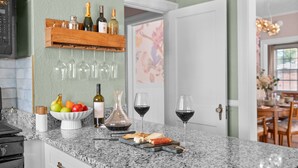 A kitchen with a granite countertop, wine bottles, glasses, a fruit bowl, and a cheese board. - Renovated 2BR w/Porch & Pool Table • San Marco (Jacksonville)
