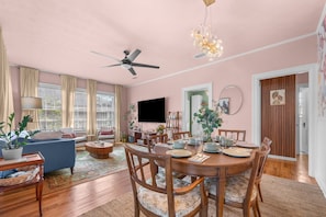 A living room with a sofa, coffee table, dining table set for four, and a TV mounted on the wall.