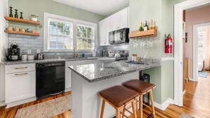 A modern kitchen with white cabinets, granite countertops, and a central island with stools. - Renovated 2BR w/Porch & Pool Table • San Marco (Jacksonville)