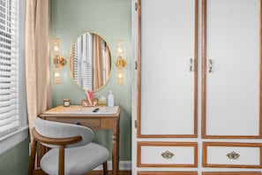 A room with a wooden desk, a chair, a mirror, wall sconces, and a wardrobe with multiple drawers.